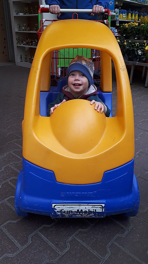 Mika im Kinderauto-Einkaufswagen im Baumarkt